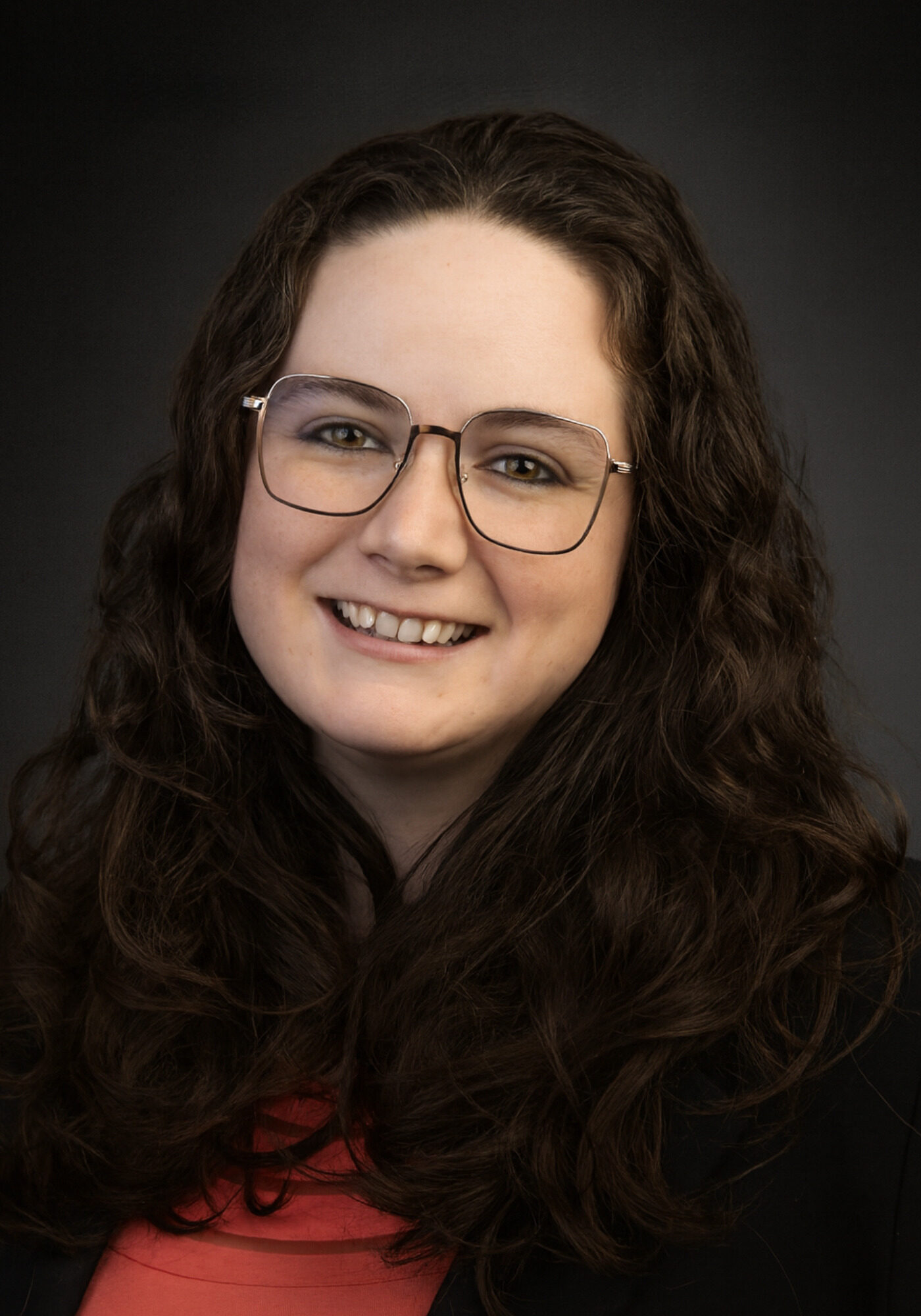 A girl with curly dark hair and glasses smiles at the camera